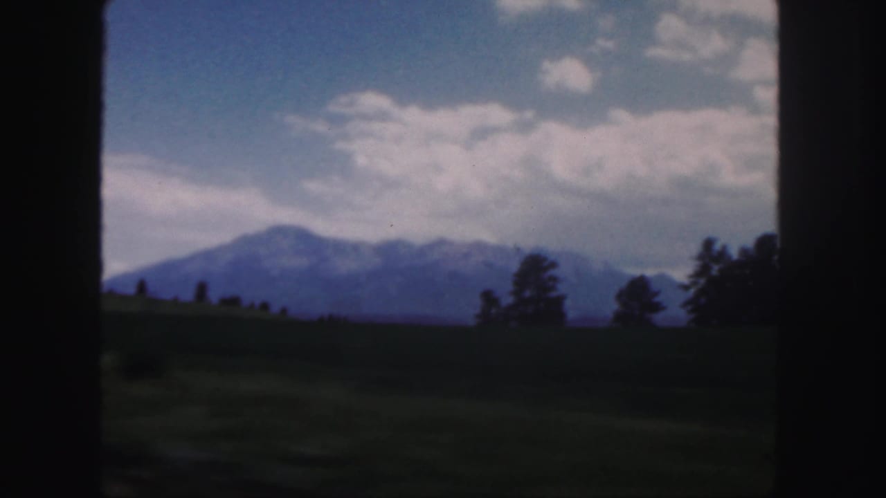 Distant mountains beyond grassy fields under a blue, cloud-filled sky.