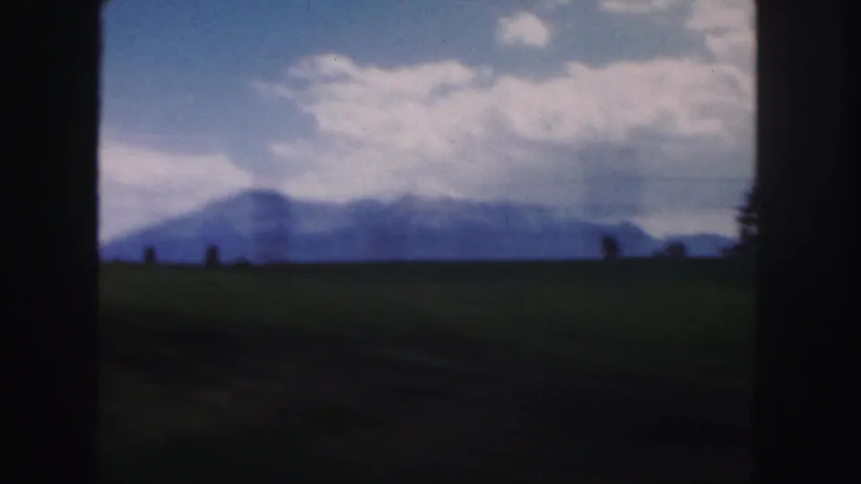1958 Colorado landscape frame with hazy blue mountains, a low grassy horizon, cloud cover, and dark vertical frame edges.