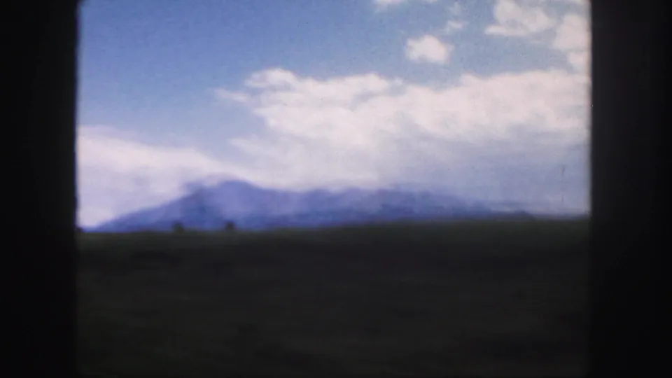 Soft 8mm view of a Colorado mountain silhouette under a bright cloud bank, with dark foreground from the moving view.