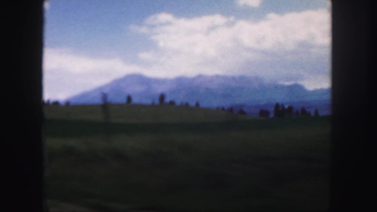 1958 Colorado home-movie frame showing hazy mountains, green foreground land, clouds, and dark contact-sheet borders.