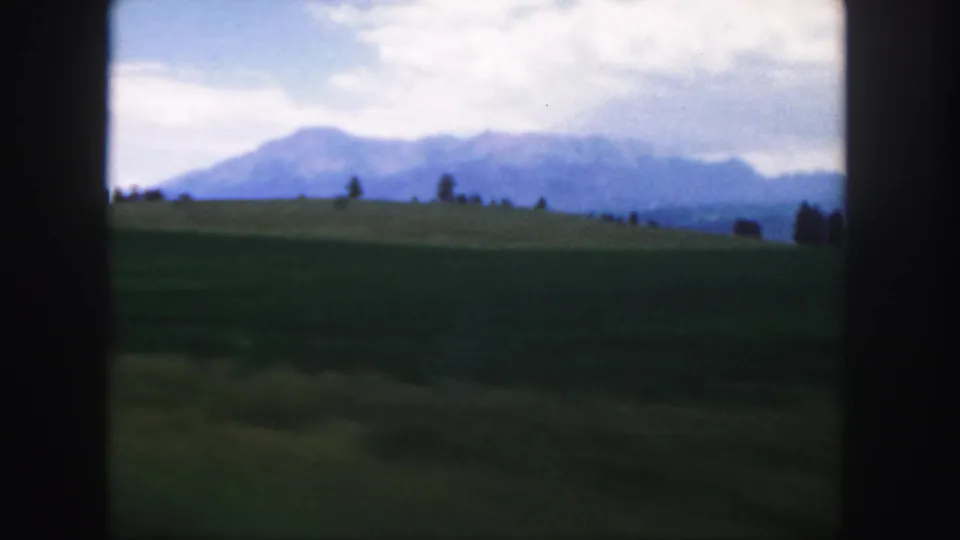 Colorado mountain landscape with a green ridge, distant blue peaks, scattered trees, and soft 8mm color rendering.