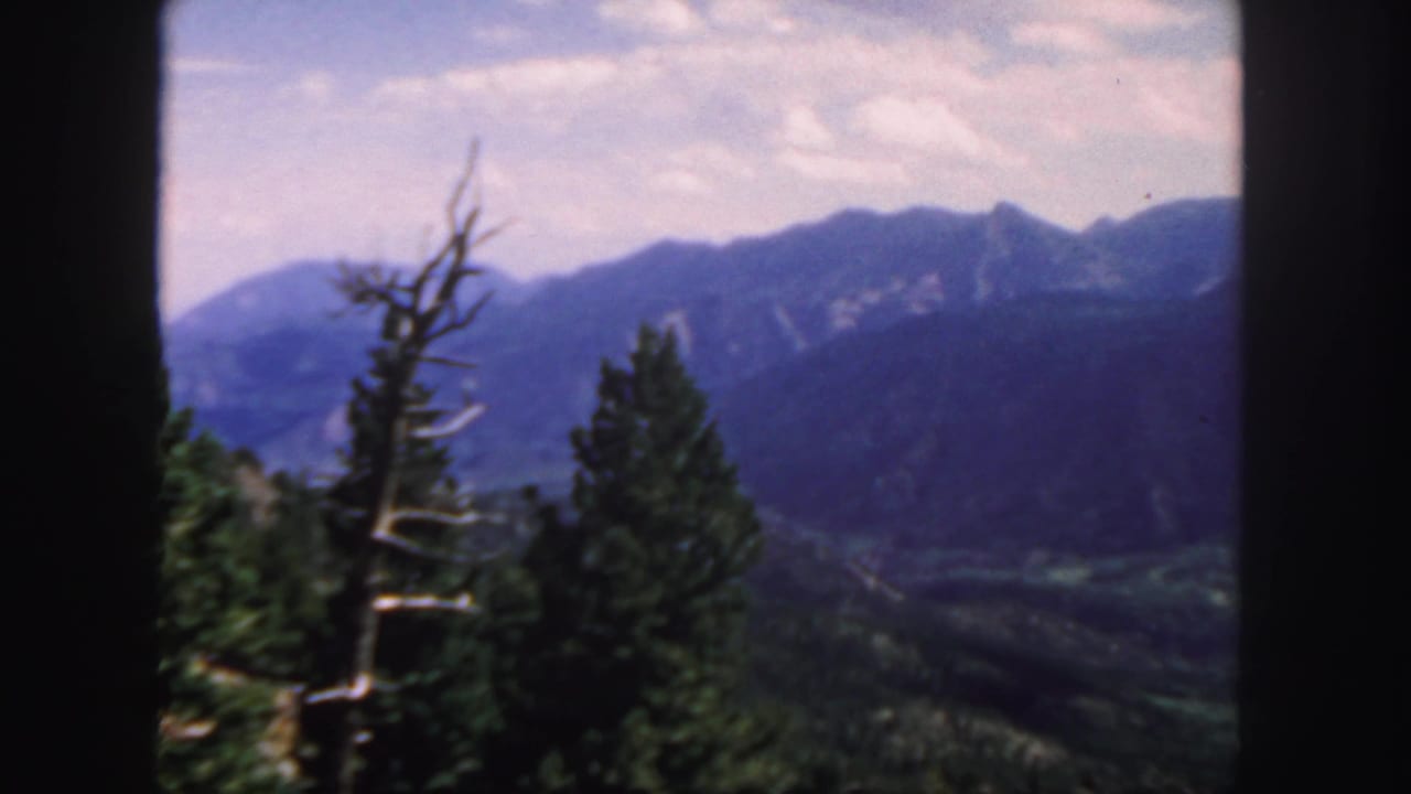 Distant mountain ridge and valley seen between dark film borders and foreground trees.