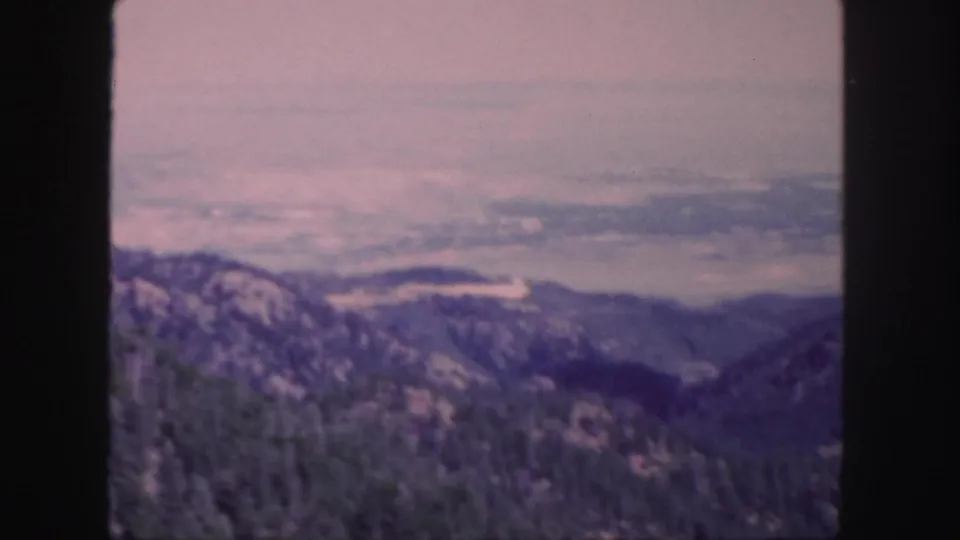1958 Colorado 8mm frame showing wooded mountain slopes and a distant hazy valley under a pale sky.