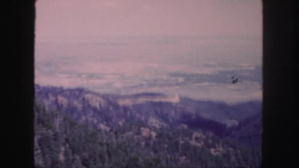 1958 Colorado 8mm frame showing forested hills, distant ridgelines, pale haze, and dark film gate borders.