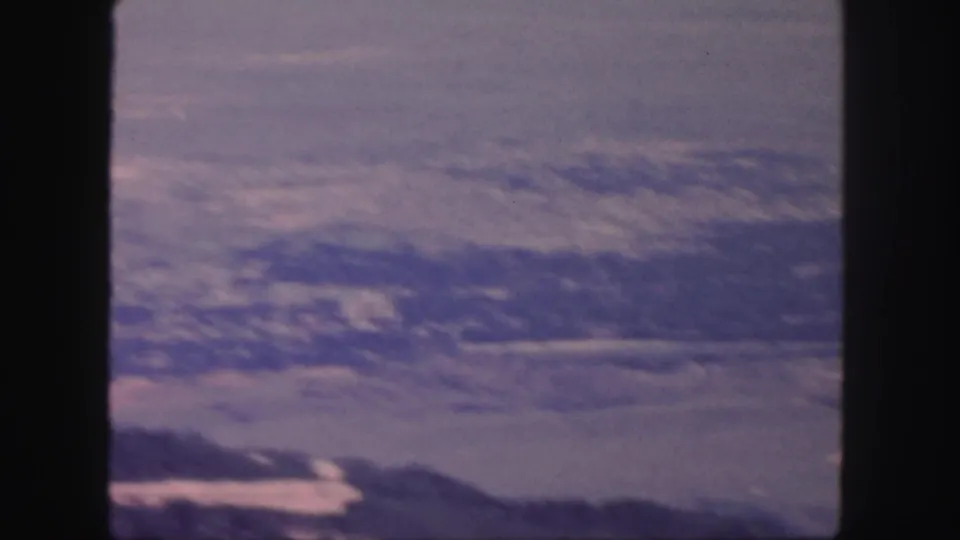 1958 Colorado home-movie frame showing a wide valley, low mountain silhouettes, and faded blue-purple film color.