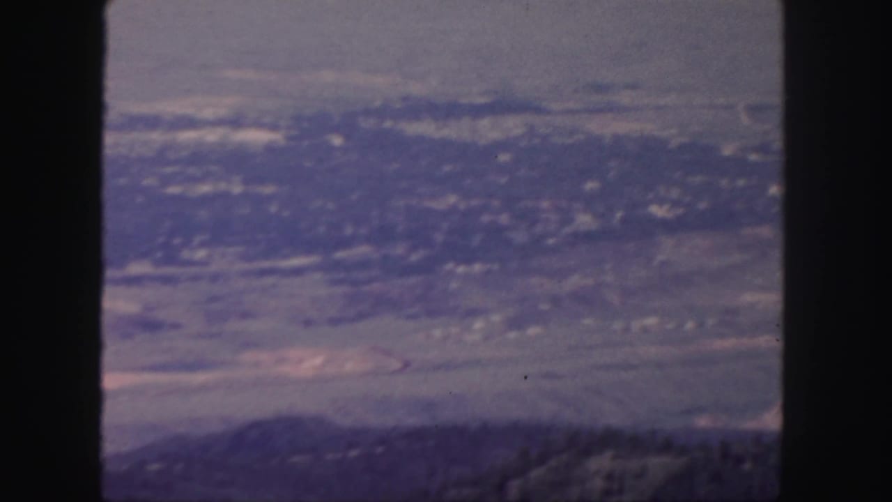 1958 Colorado 8mm frame looking over a hazy valley and distant hills from an elevated viewpoint.