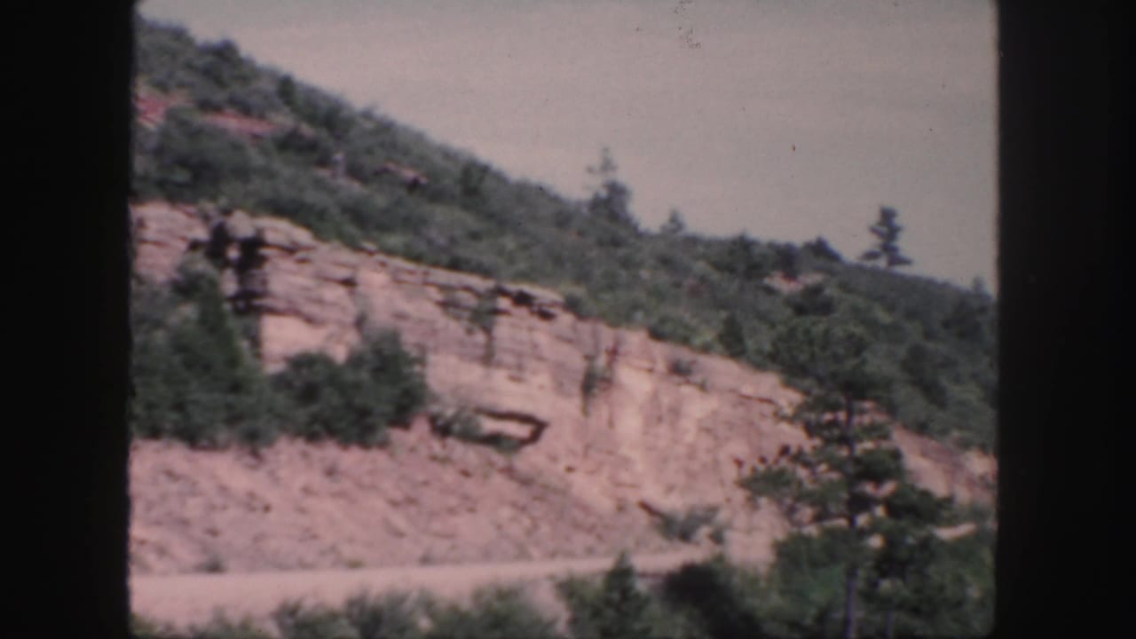 Rocky mountain slope with trees and a road or shoulder below.