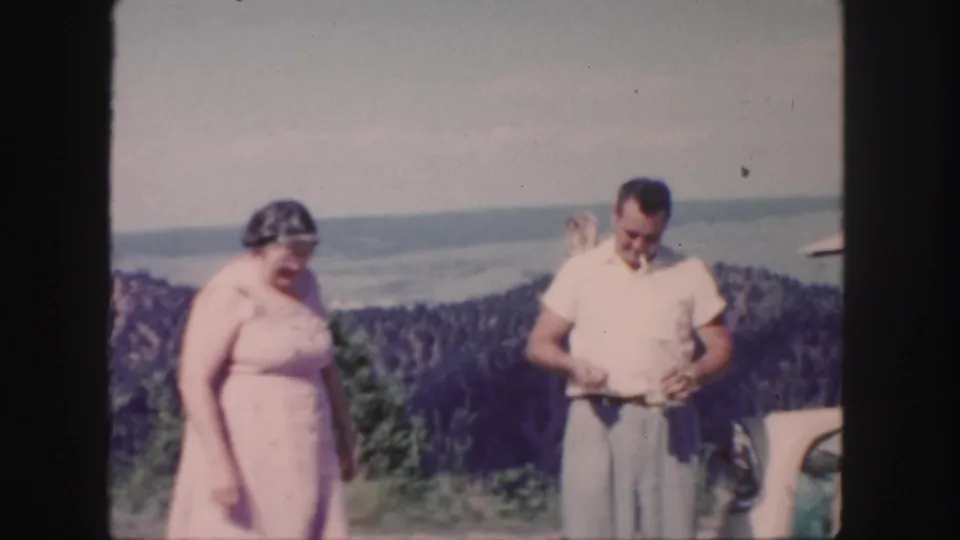 1958 Colorado frame showing the couple beside the open trunk, with the man looking down and the woman standing near him at the overlook.