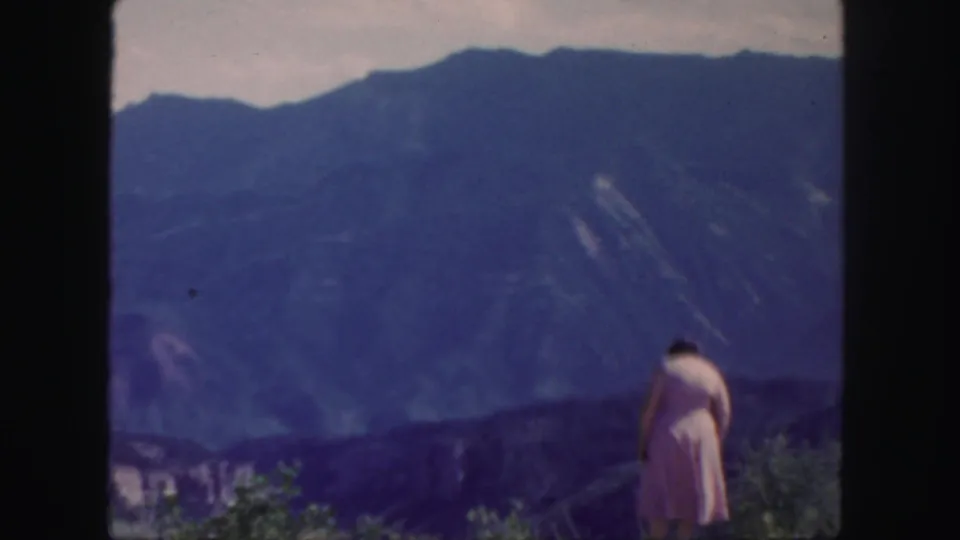 A woman in a pink dress looks out over blue mountain ranges in Colorado, framed by soft 8mm color and dark film borders.