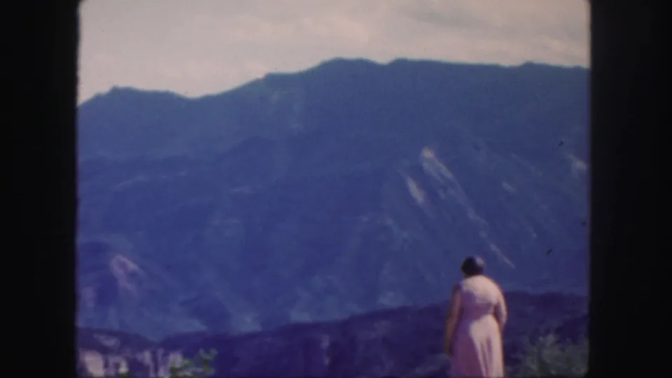 The woman stands alone at the overlook, her pink dress visible against the distant Colorado mountain ridges.