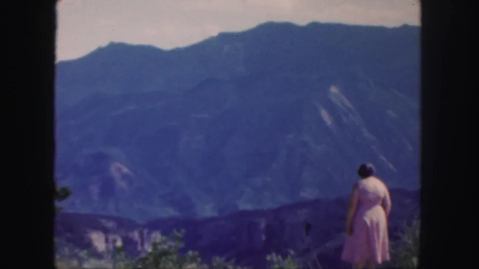 A wide 8mm frame places the woman at the edge of the overlook with blue Colorado mountains filling the background.