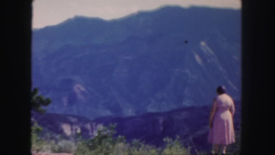 The woman remains near the right side of the 1958 Colorado frame, looking toward layered blue mountain ridges.