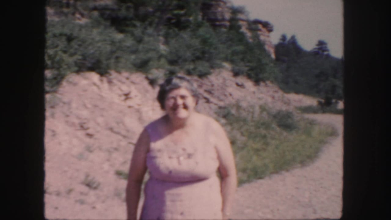 Woman in a light dress smiling on a dirt path with brush and trees behind her.