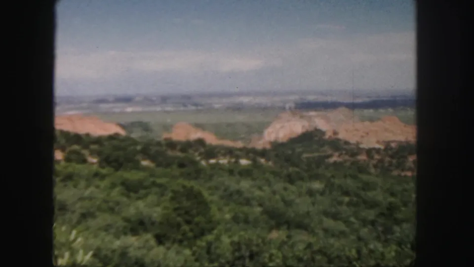 Colorado home-movie landscape frame with wooded hills, pale rock outcrops, a distant valley, and hazy sky.