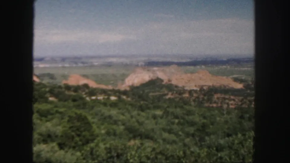 1958 Colorado 8mm frame with dark film borders around a hazy view of green hills, reddish rock formations, valley, and sky.