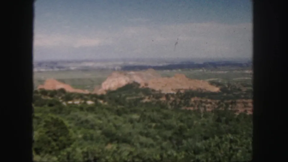 Final 1958 Colorado frame showing a wide home-movie view of green hills, reddish rock formations, distant terrain, pale sky, and dark film edge.