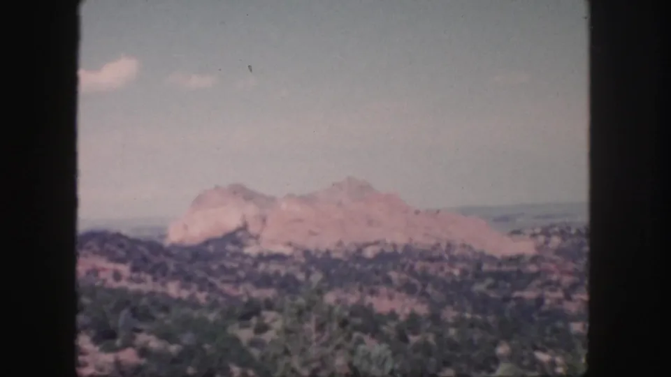 1958 Colorado home-movie frame showing a closer red rock formation rising behind scrub-covered hills, with faded color and grain.