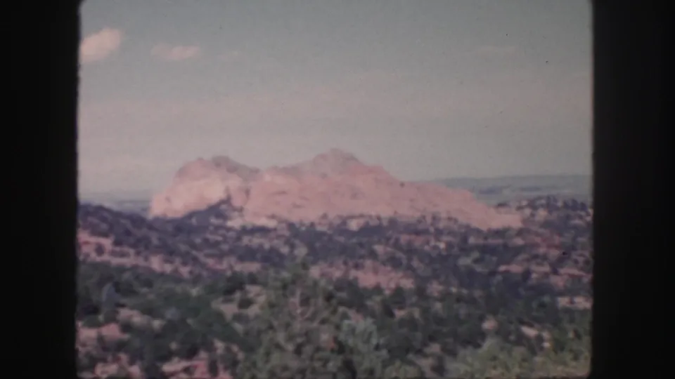 Color 8mm frame from Colorado showing red rock formations, green brush in the foreground, and a softly faded sky.