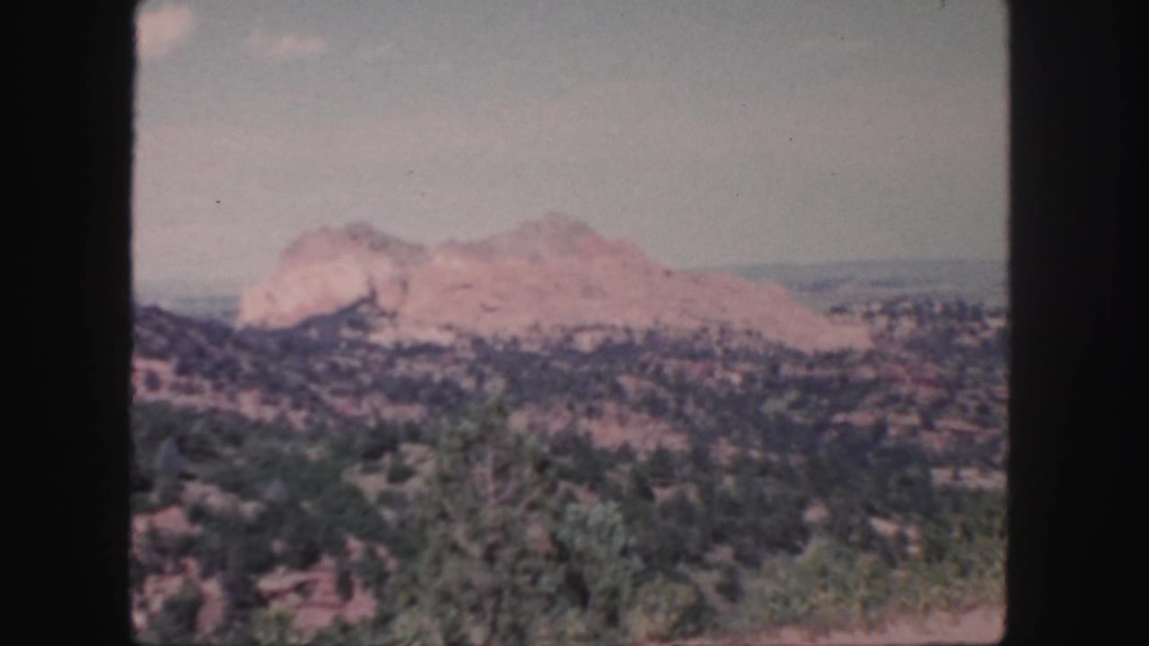 Rocky mountain formation seen across dry vegetation and distant terrain.