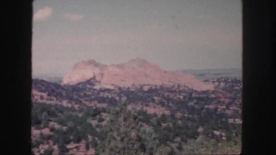 1958 Colorado 8mm frame showing distant rocky mountains over dry scrubland, with faded color and visible film texture.