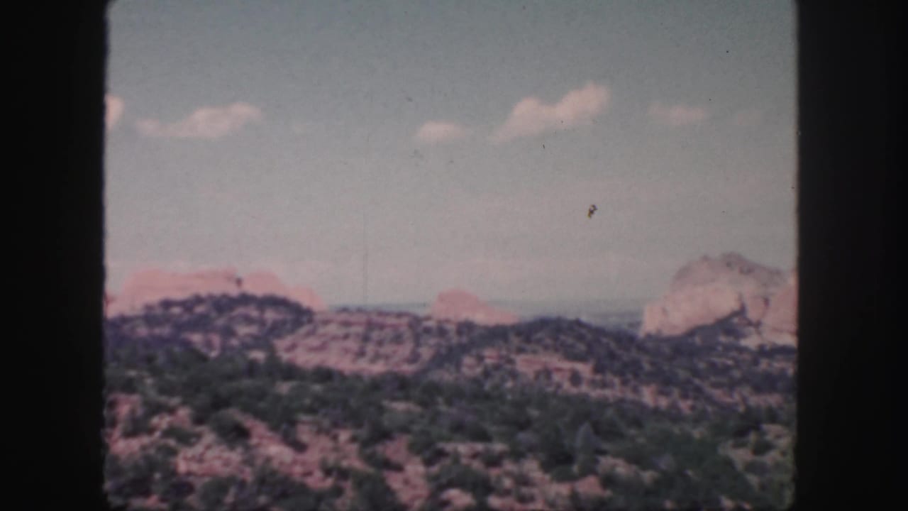 Soft 8mm view of dry rocky hills under a pale blue sky with small clouds.