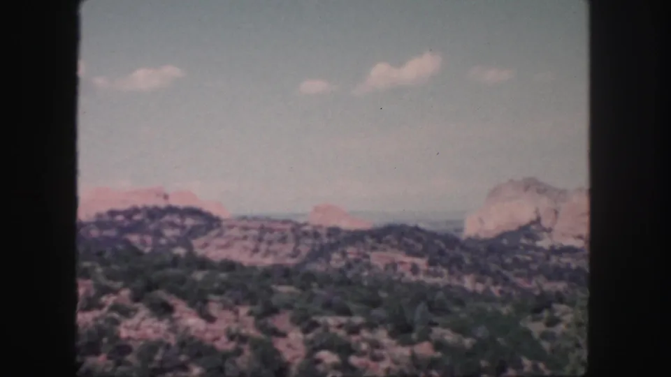 1958 Colorado 8mm frame with red and tan rock formations, scrubby ridges, and a softly exposed sky.