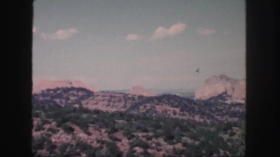 Colorado desert landscape on 8mm film, showing dry brush, dark ridges, red rock, and a light cliff at right.