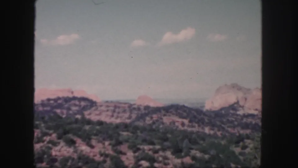 1958 Colorado home-movie still with scrub-covered hills, red rock formations, and soft 8mm color exposure.