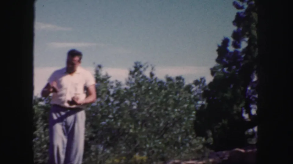 The man stands with fruit in his hands, surrounded by orchard foliage and open sky in the 1958 Colorado clip.