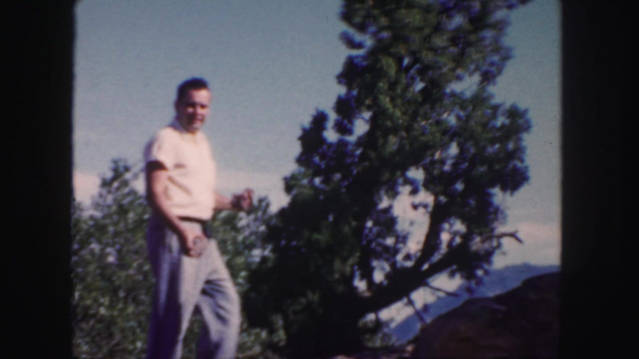 A smiling man in light clothing walks through a Colorado mountain setting in color 8mm home-movie footage from 1958.
