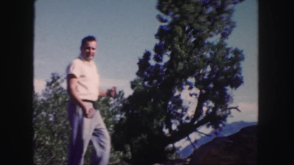 A smiling man in light clothing walks through a Colorado mountain setting in color 8mm home-movie footage from 1958.