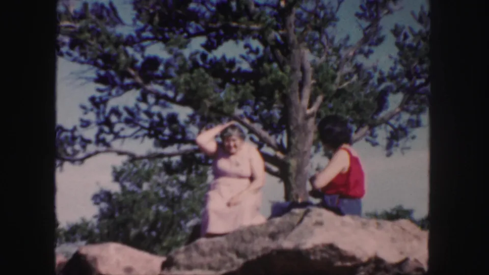 1958 Colorado 8mm frame showing a seated woman gesturing beside another woman on a mountain rock.