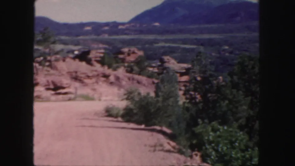 A dry dirt road runs through Colorado scrub and red rock terrain toward distant mountains in 1958 8mm footage.