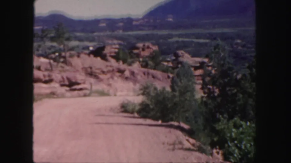 The road and roadside vegetation frame a Western Colorado landscape of red rock outcrops, valley floor, and mountains.