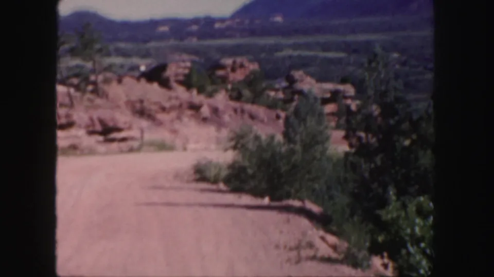 Colorado 8mm travel footage shows a pale dirt road beside red sandstone, scrub vegetation, and hazy mountain ridges.