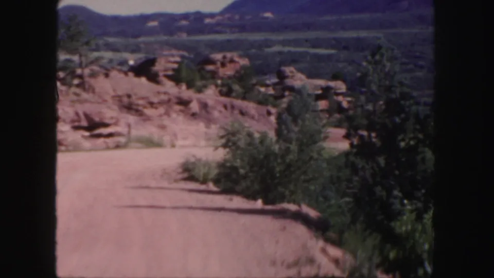 The 1958 Colorado travel shot continues across a dirt road, red rock outcrops, trees, and distant mountains.