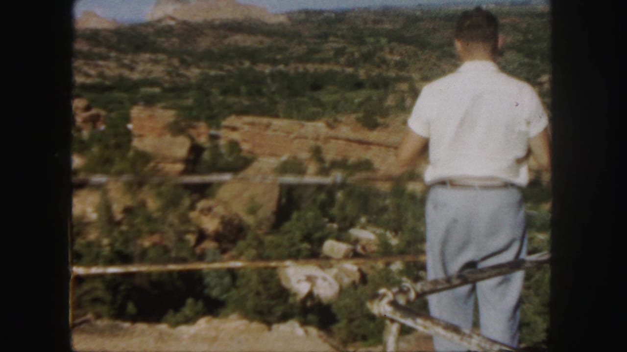 In Colorado home-movie footage from 1958, a man stands with his back to camera at a scenic canyon overlook.