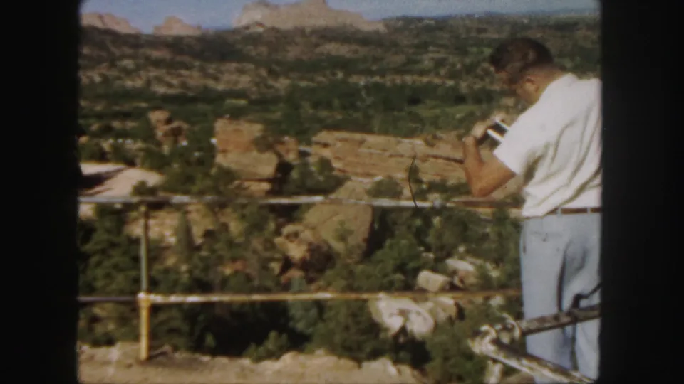At the end of the 1958 Colorado clip, the man remains at the overlook with binoculars aimed across the canyon.
