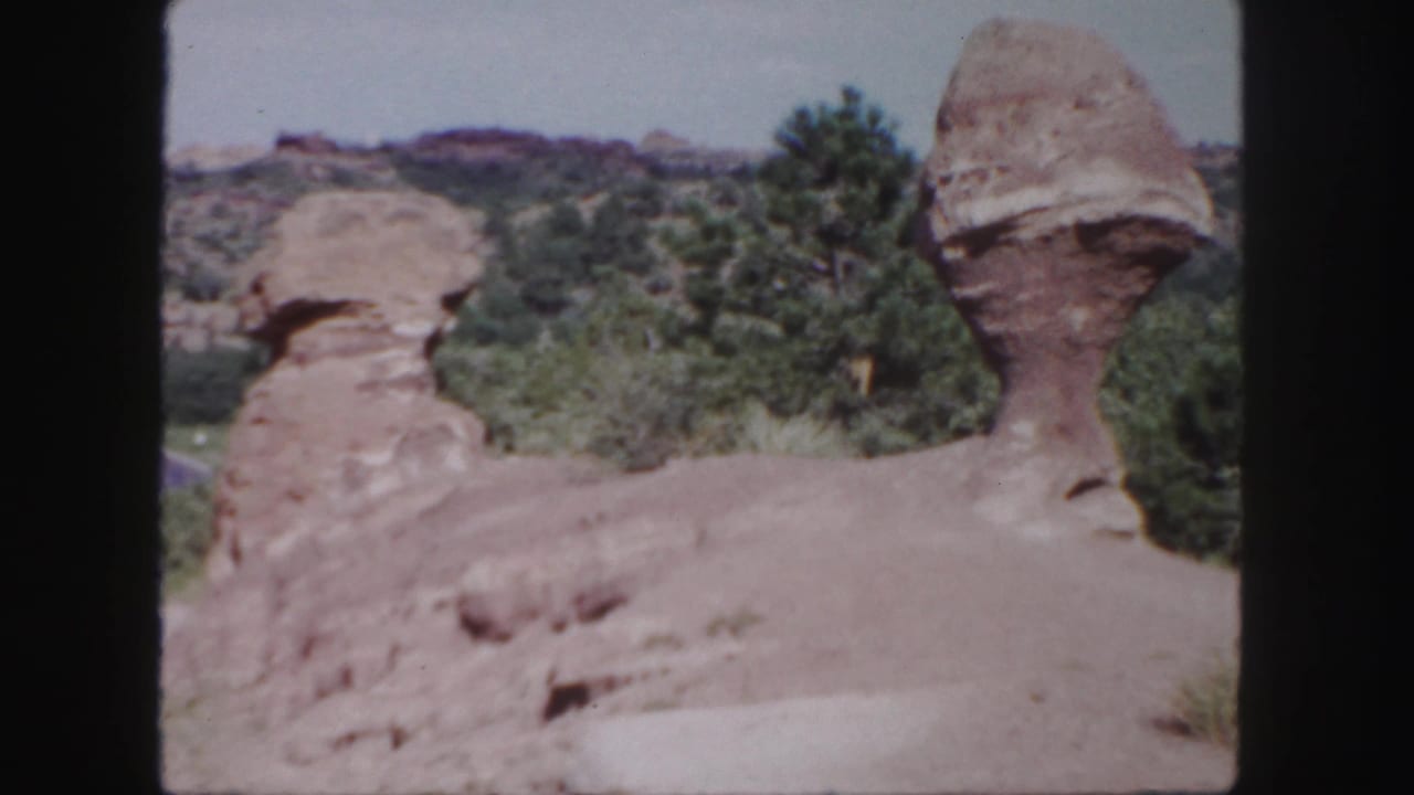 1958 Colorado 8mm frame showing two distinctive red rock formations beside trees under a pale sky.