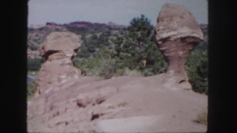 1958 Colorado 8mm frame showing two distinctive red rock formations beside trees under a pale sky.