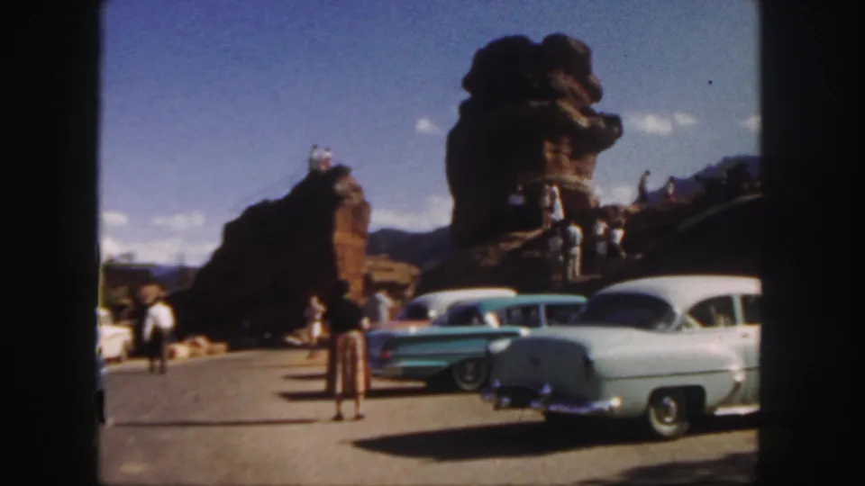 Colorado travel footage frame with visitors near late-1950s cars and sculptural red rock formations in bright daylight.