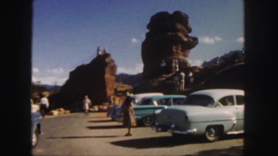 1958 Colorado 8mm frame showing a scenic tourist stop with cars, pedestrians, and large weathered red rock outcrops.