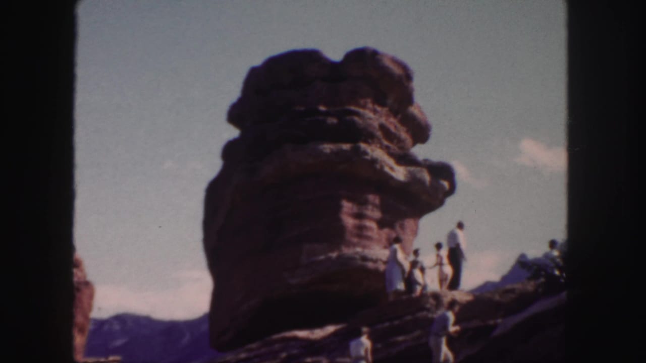 Visitors stand on a large red sandstone formation under a bright sky.