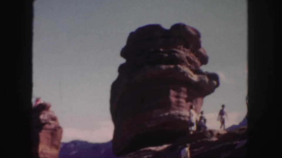Soft 8mm view of a Colorado red sandstone formation with visitors scattered around the rock ledge and mountains in the distance.