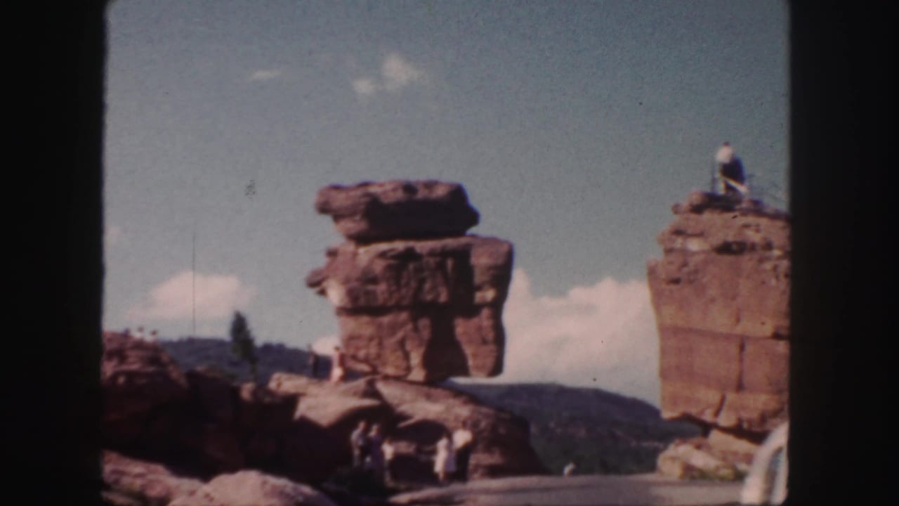 1958 Colorado 8mm frame showing red rock formations, distant mountains, visitors below, and a man on a high ledge.