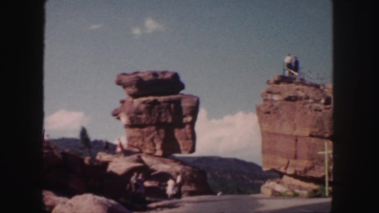 Two red rock formations beside a paved path, with a man on the right formation.