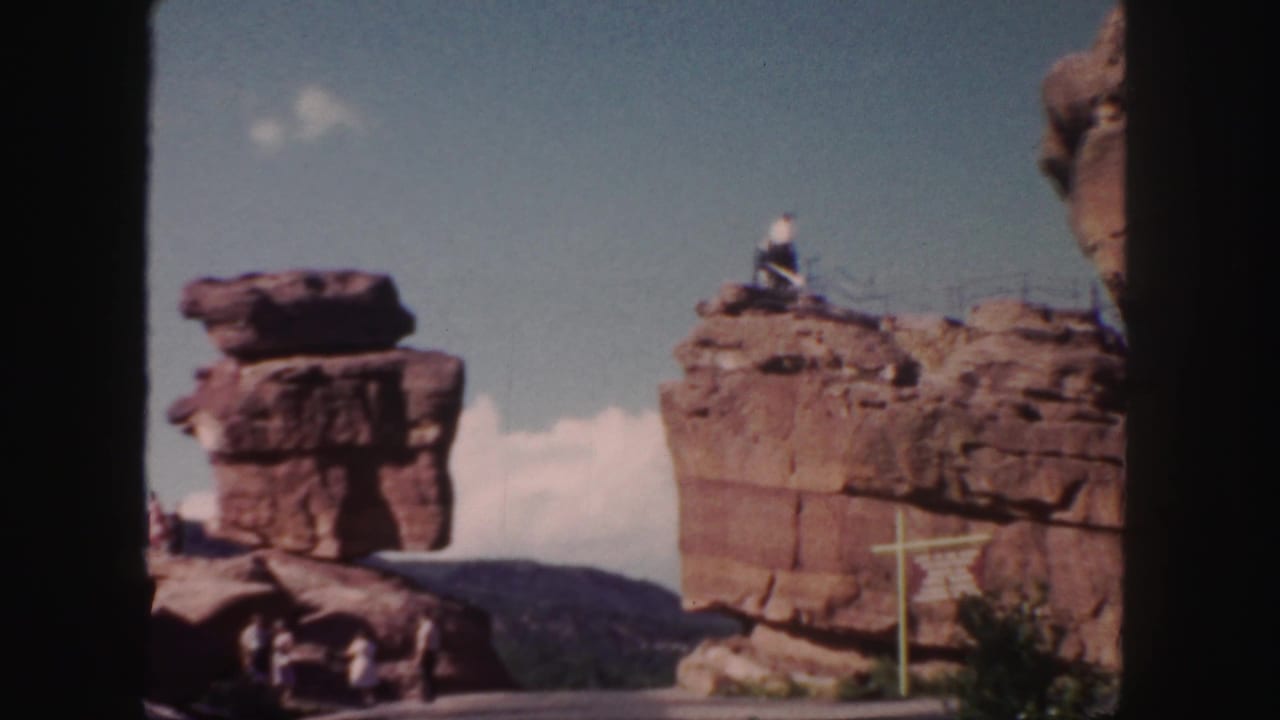 Red rock formations beside a roadside signpost under a blue sky.