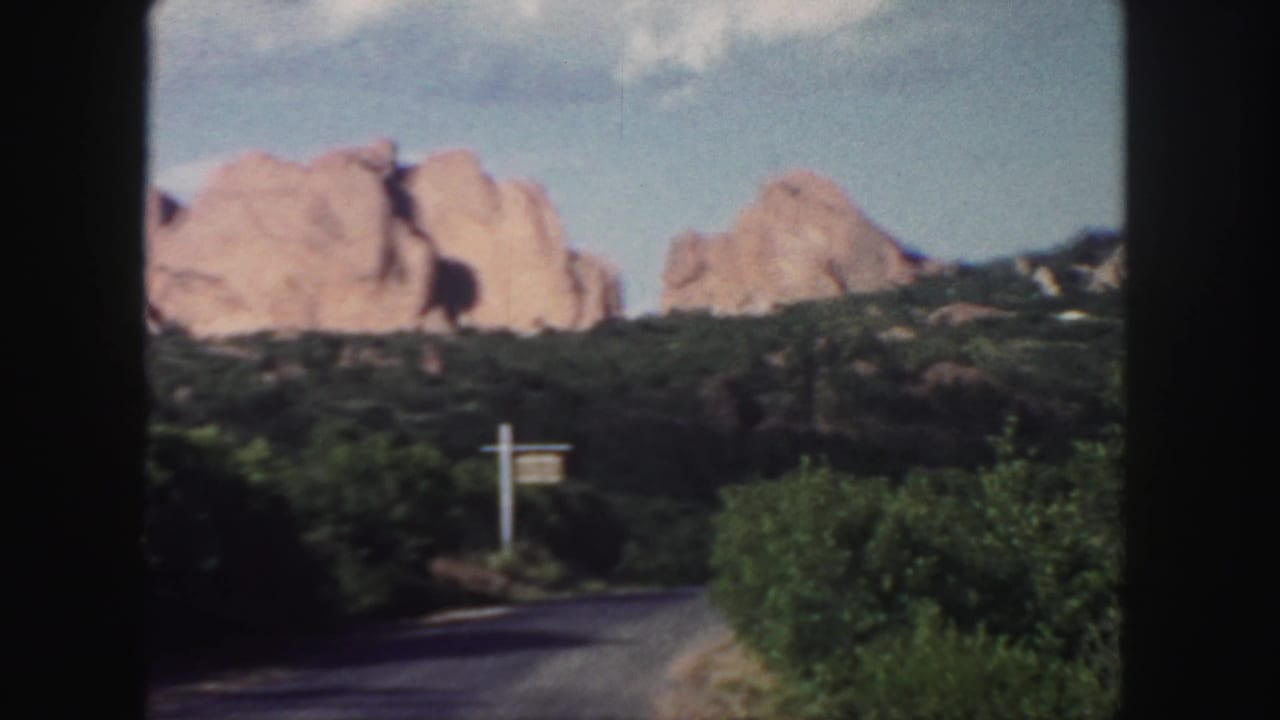 Paved road curves toward red rock formations and a white signpost.