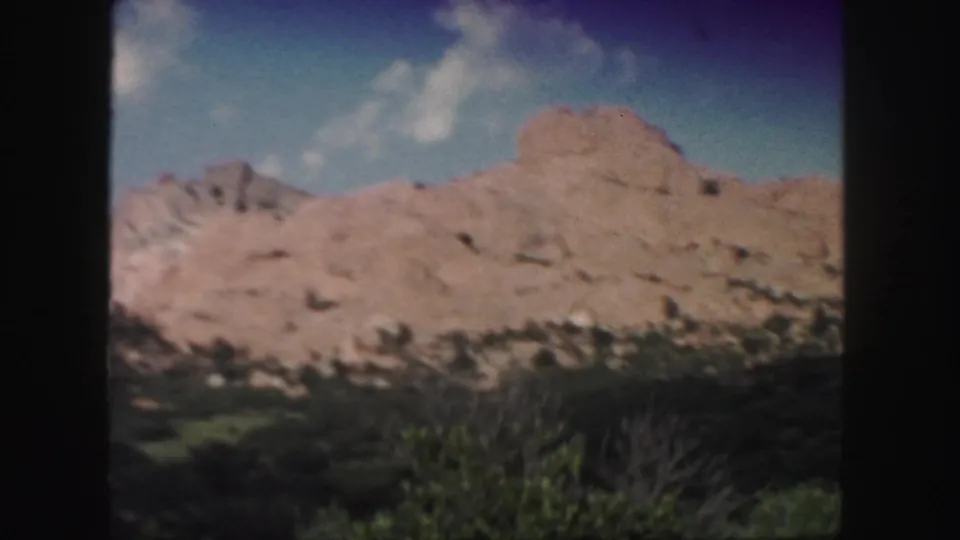 1958 Colorado 8mm frame showing a broad tan cliff face with green trees and brush in the foreground.