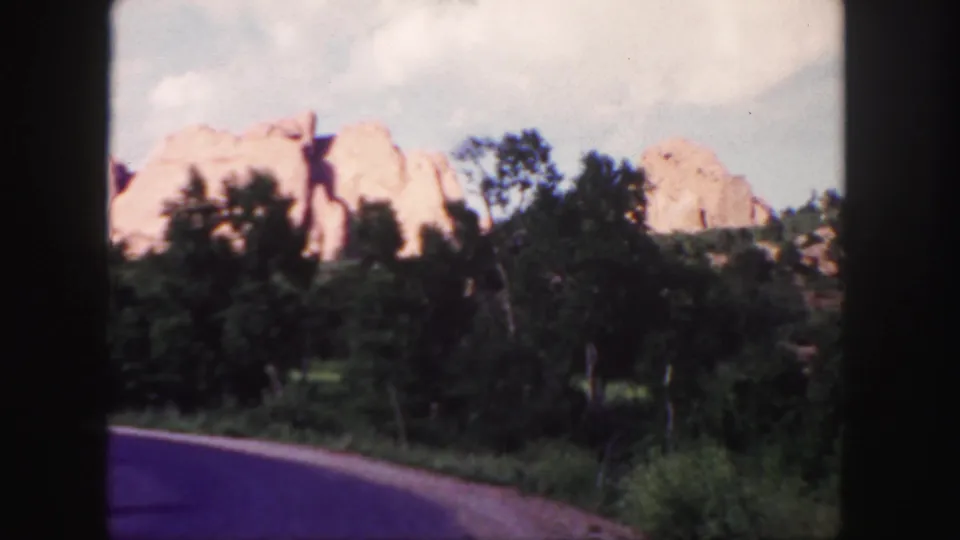 1958 Colorado 8mm frame looking past a bend in the road toward trees and red rock formations after the car has passed.